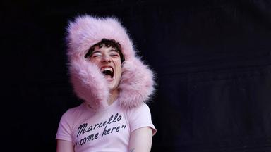 Nonbinäre Person trägt pinkfarbene Pelzmütze