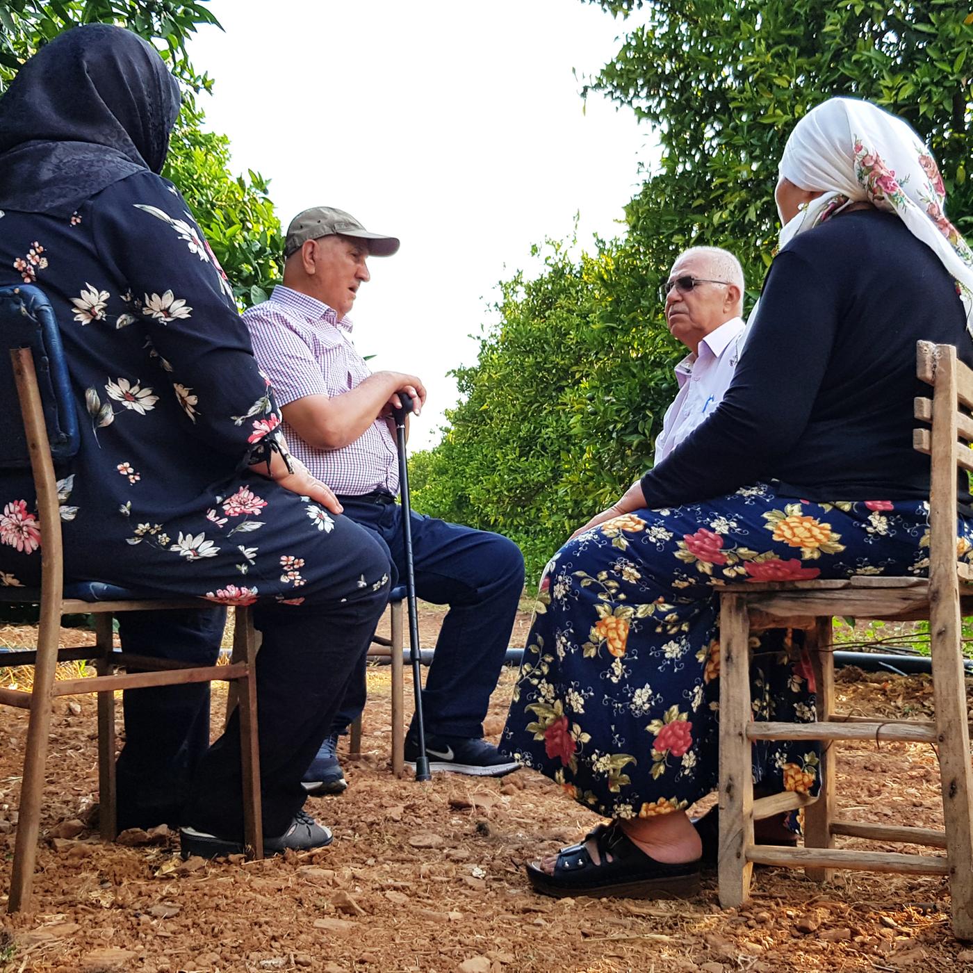 Zwei ehemalige Gastarbeiter sitzen mit ihren Ehefrauen inmitten einer Orangenplantage in der Türkei und unterhalten sich.