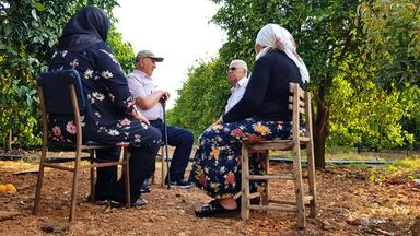 Zwei ehemalige Gastarbeiter sitzen mit ihren Ehefrauen inmitten einer Orangenplantage in der Türkei und unterhalten sich.