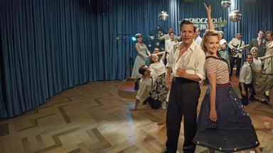 "Ku'damm 59": Monika Schöllack (Sonja Gerhardt, m.r.) und Freddy Donath (Trystan Pütter, m.l.) stehen im Vordergrund und posieren für die Kamera. Im Hintergrund posieren weitere Darsteller der Fernsehshow "Rendezvous nach Noten".