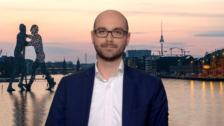 Mann mit Brille vor einer Berlin-Skyline bei Sonnenuntergang.