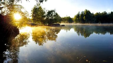 Die untergehende Sonne spiegelt sich in einem ruhigen See.