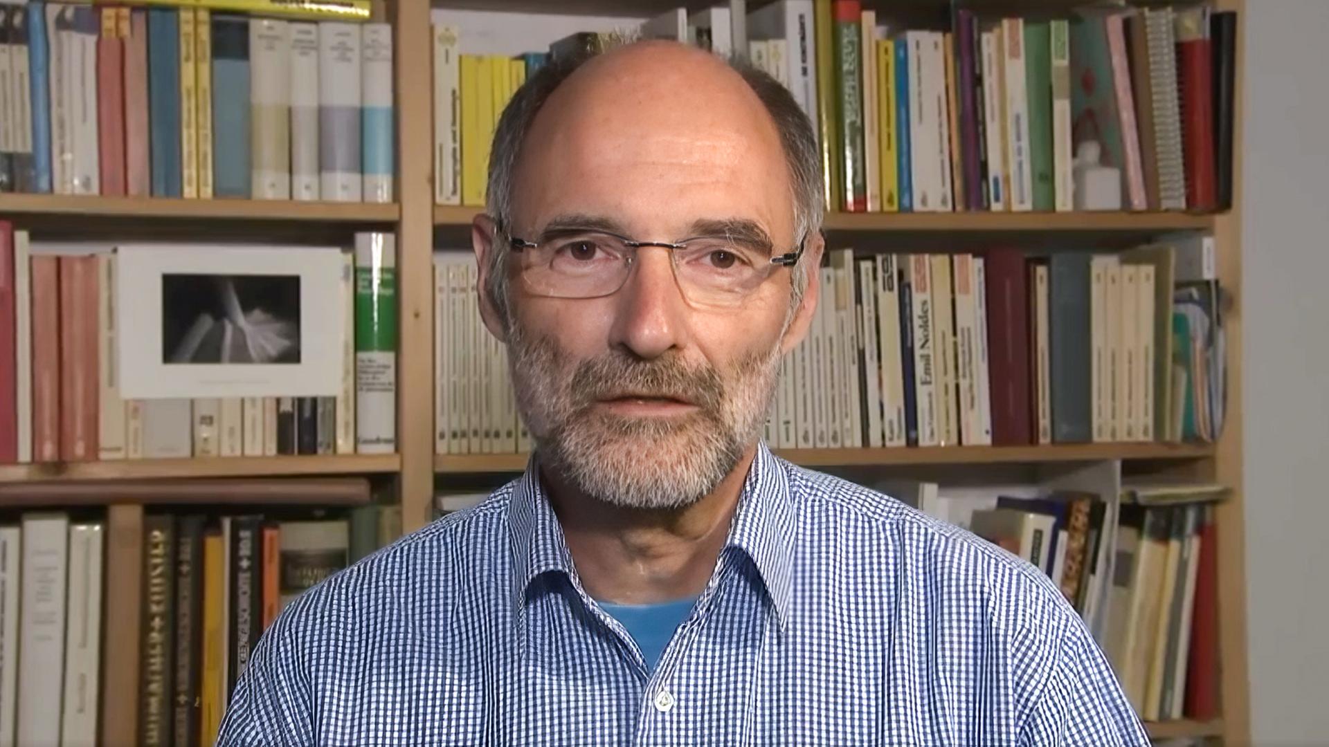 Peter Nussbaum sitzt vor einem Bücherregal.