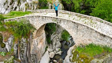 Eine Frau auf einer Steinbrücke in einer Berglandschaft.
