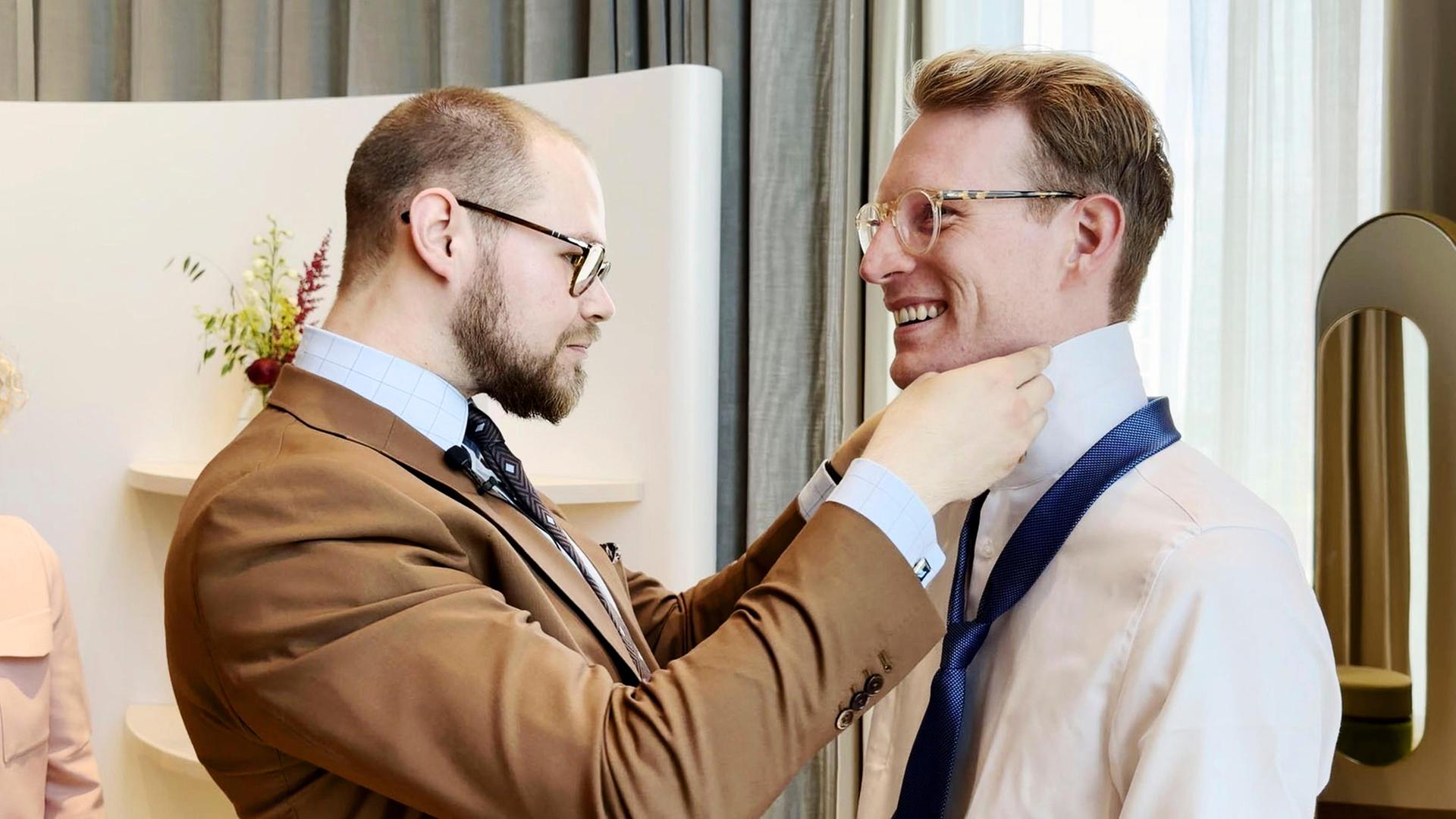 Ein Mann zeigt einem anderen Mann, wie ein Windsor-Knoten gebunden wird