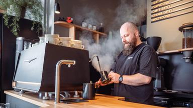 Benjamin Ooschauko, kräftig, Glatze und Vollbart, bereitet Kaffee zu.