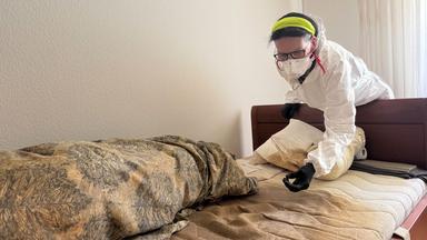 Eine Frau in Schutzanzug beugt sich über ein Bett.