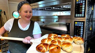 Eine junge Frau mit einer Backschaufel mit Brötchen.