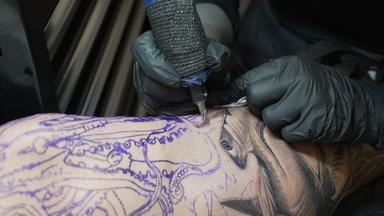 Nahaufnahme eines Tattoovorgangs auf einem Schienbein.