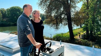 Ein Paar am Steuer eines Hausbootes.