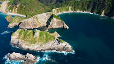 Luftaufnahme des Strands der Stille bei Cudillero in Asturien mit steilen, grün bewachsenen Felsen, kleinen Buchten und dunkelblauem Meer.