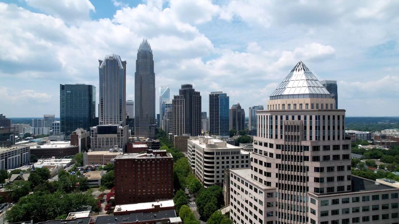 Skyline der Stadt Charlotte im North Carolina. Im Vordergrund steht ein Hochhaus mit einem markanten Spitzdach, im Hintergrund sind zahlreiche weitere Hochhäuser zu erkennen.