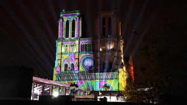 Die Kathedrale Notre Dame de Paris wird bei Nacht mit bunten Lichtern angestrahl.