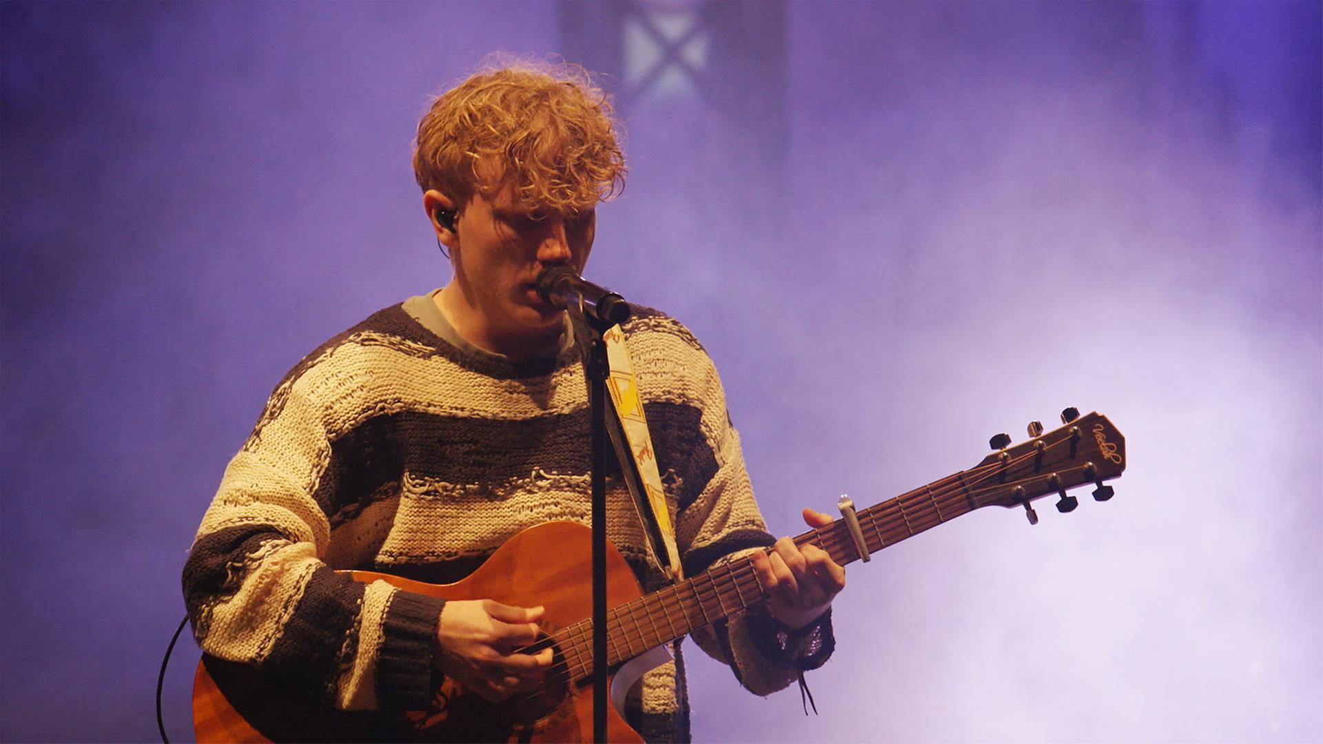 Indie-Pop-Sänger TJARK mit Gitarre vor Mikrophon auf der Bühne