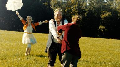 Karoline Schuch mit Schirm in der Hand, Aljoscha Stadelmann und Lars Rudolph Fuchs tanzen auf einer Wiese