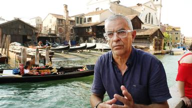 ein mann sitzt vor einem gewaesser mit booten und haeusern im hintergrund