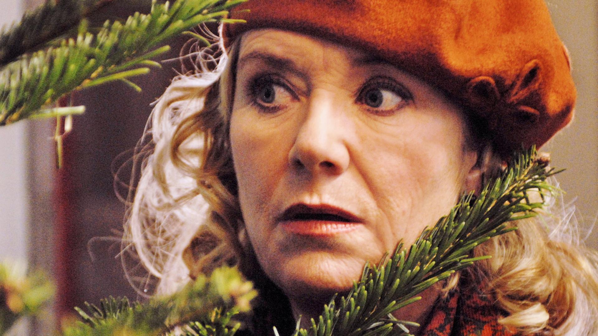 Rita (Jutta Speidel) versteckt sich hinter einem Weihnachtsbaum