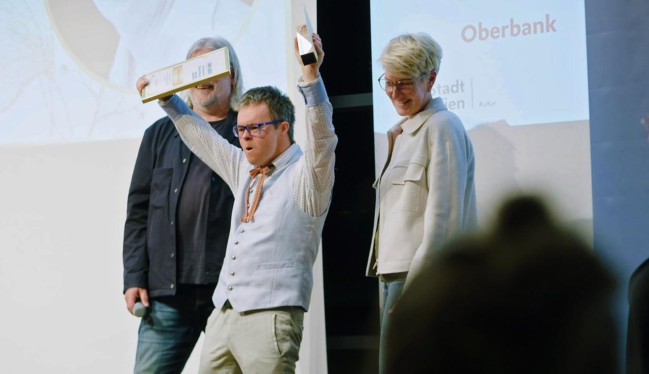 Ein junger Mann streckt seinen Preis und seine dazugehörige Urkunde vor Freude in die Höhe