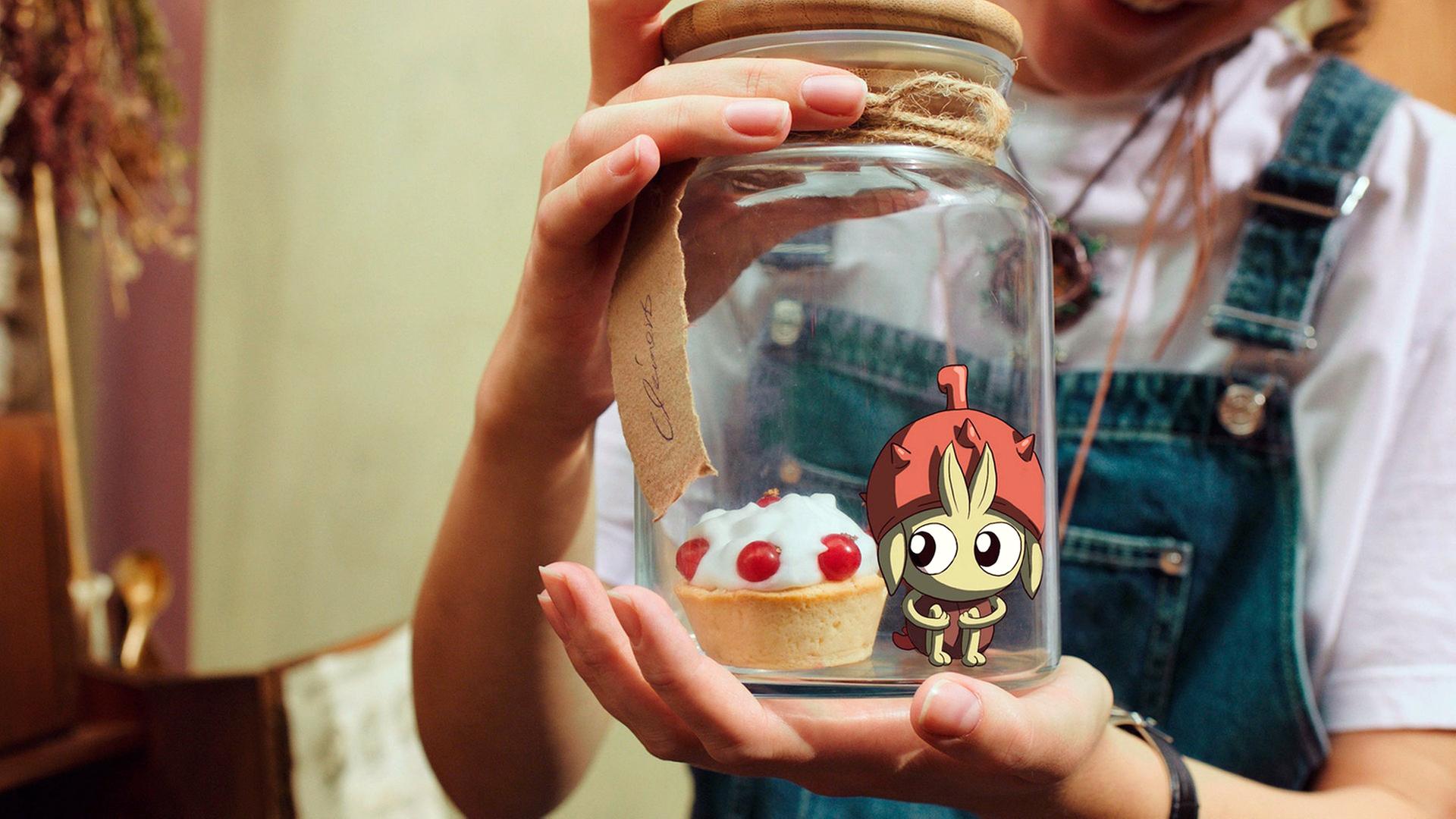 Eine Frau mit Latzhose hält ein Glas mit einem Törtchen und einer kleinen Figur in den Händen.