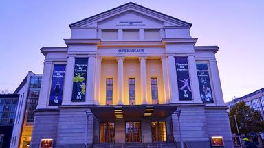 Beleuchtete Fassade eines historischen Opernhauses in der Abenddämmerung.