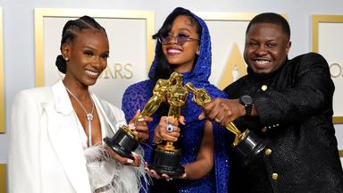 Zwei schwarze Frauen und ein Mann in festlich-glitzernder Kleidung halten lachend drei goldene Oscar-Statuen.
