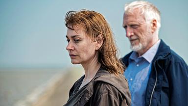 Frau am Strand schaut betroffen zu Boden