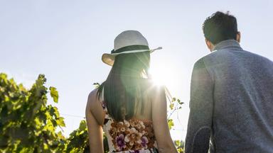 Eine junge Frau mit Sonnenhut und ein Mann laufen Händchenhaltend an einem sonnigen Tag im Grünen.
