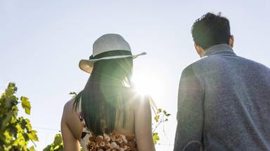 Eine junge Frau mit Sonnenhut und ein Mann laufen Händchenhaltend an einem sonnigen Tag im Grünen.