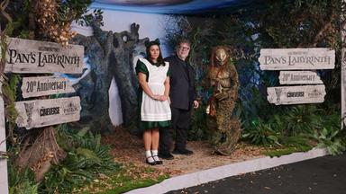 Regissur Guilermo del Toro und zwei Darsteller, win Mädchen und eine Fantasyfigur stehen in einer waldartigen Kulisse.