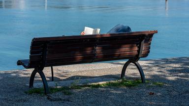 Mensch liegt auf Parkbank und liest
