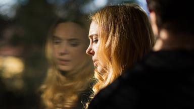 Eine Frau lehnt ihren Kopf an eine Fensterscheibe, in der sich ihr verzweifeltes Gesicht spiegelt.