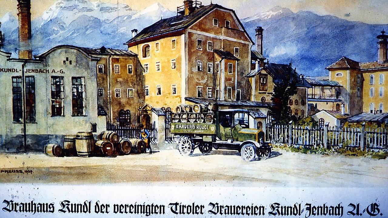 Das Bild zeigt eine historische Bierbrauerei in Kundl mit mehreren Gebäuden und einem alten Lkw, der mit Bierfässern beladen ist. Im Hintergrund sind Berge sichtbar.