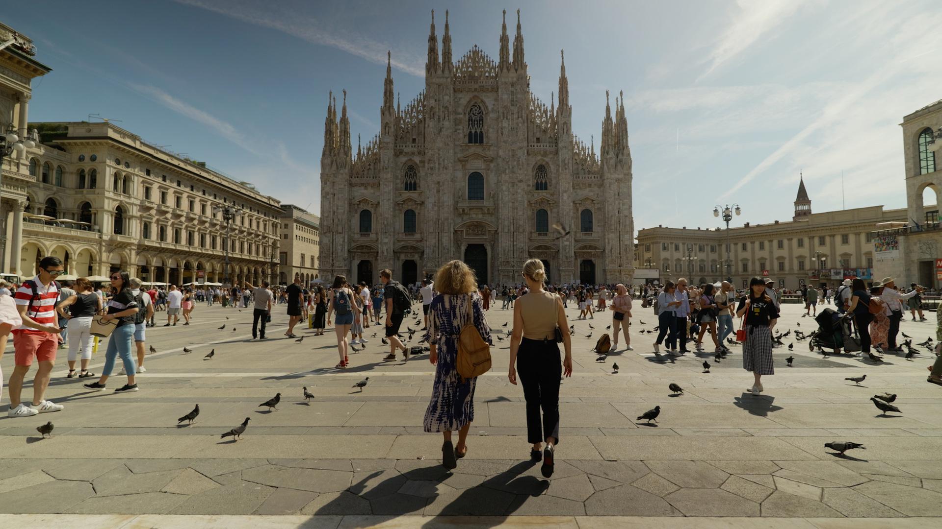 Zwei Frauen laufen mit dem Rücken zur Kamera auf den Mailänder Dom zu.