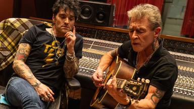 Peter Maffay sitzt auf einem Stuhl, spielt Gitarre und singt. Hinter ihm ist ein großes Mischpult und neben ihm sitzt ein Mann, der Peter Maffay anschaut.