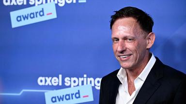 Porträtfoto eines Mannes vor einer blauen Wand mit dem Logo Axel Springer Award.