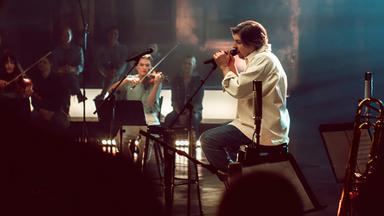 Der Sänger Philipp Poisel sitzt auf der Bühne und singt in ein Mikro.