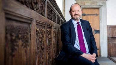 Ein Mann sitzt auf einer alten, kunstvoll geschnitzten Holzbank