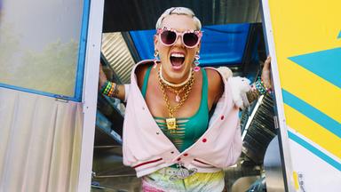 P!nk steht an einer Tür mit weit geöffnetem Mund und schrillem, bunten Outfit.