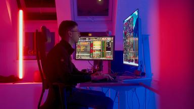 Ein junger Mann an einem Schreibtisch mit mehreren PC-Bildschirmen.