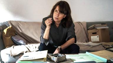 Brasch (Claudia Michelsen) sitzt rauchend auf dem Sofa.