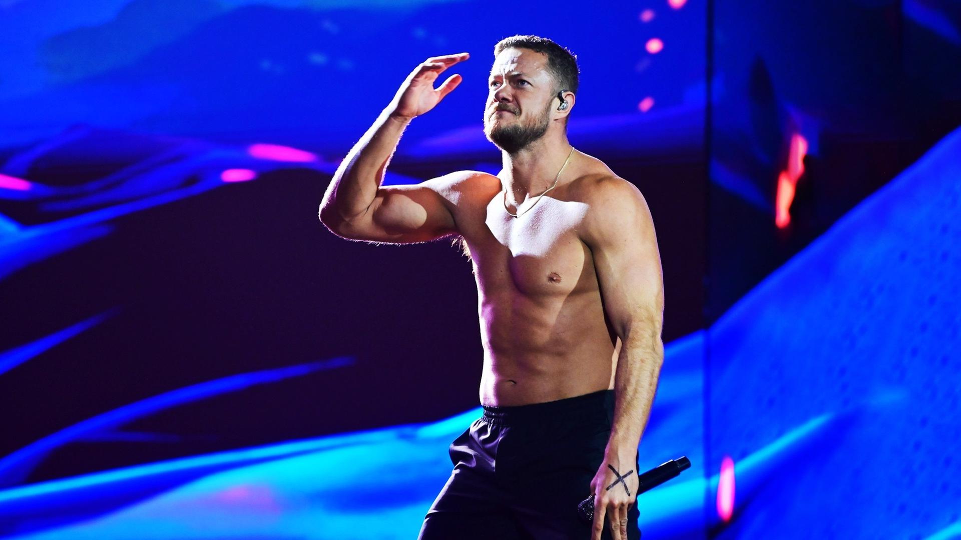 Der Sänger von Imagine Dragons steht oberkörperfrei auf der Bühne, blickt nach oben und hält seinen Arm in die Luft.