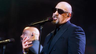 B-Real von Cypress Hill steht im schwarzen Anzug und mit Sonnenbrille auf der Bühne und singt ins Mikrofon.