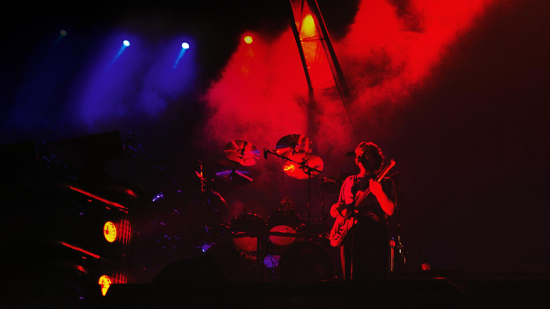 Zu sehen ist eine Bühne mit Instrumenten, viel Nebel und eine Person, die mit Gitarre am Mikrofon steht.