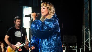 MIA steht in blauer Glitzerjacke und mit einer Hand am Mikroft auf der Bühne.