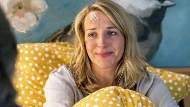 Eine Frau mit einer genähten Kopfverletzung sitzt im Bett.