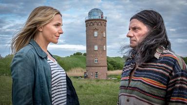 Ein Mann und eine Frau stehen sich vor einem Leuchtturm gegenüber.