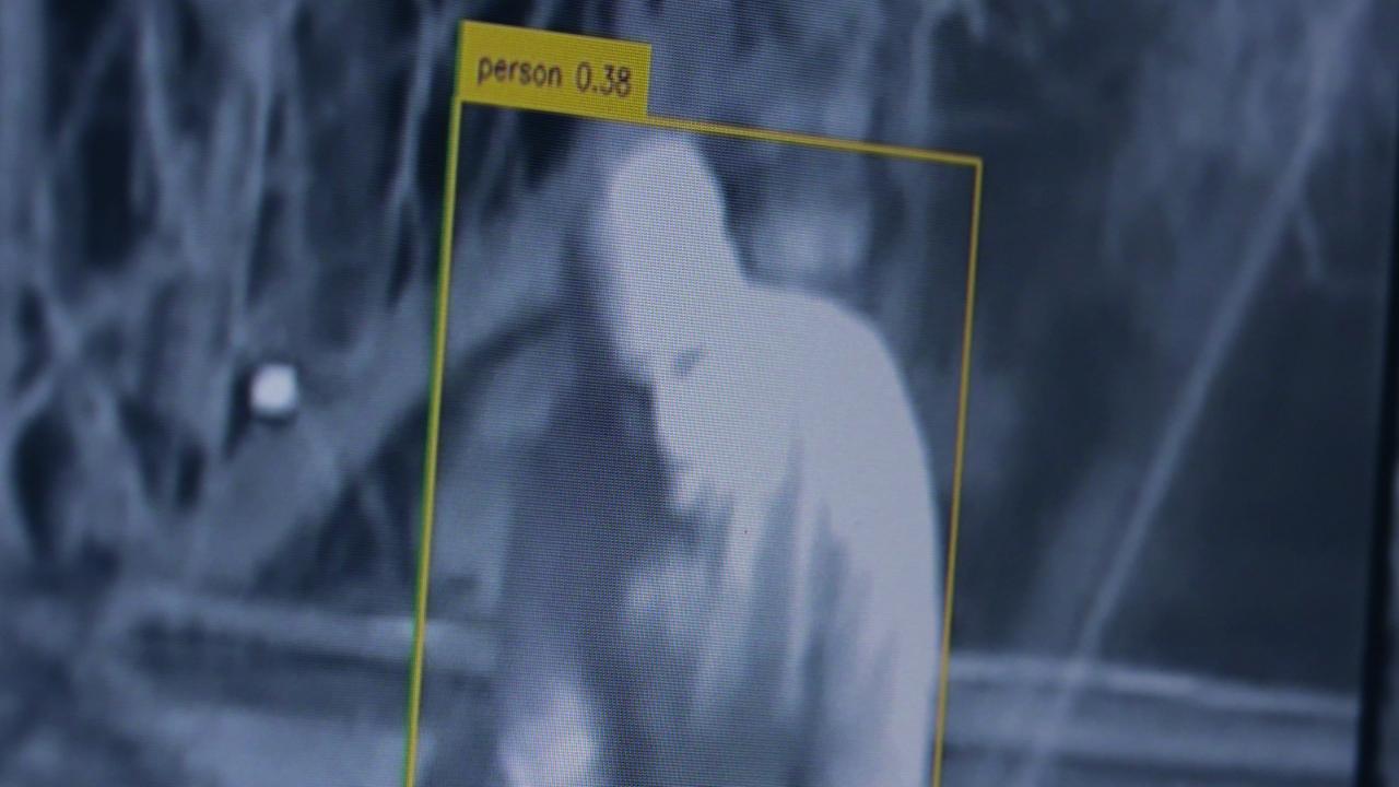 graues Negativbild einer Überwachungskamera. In der Mitte eine helle Person erkennbar, um sie herum ein gelber Rahmen mit der Bezeichnung "person 0.38".