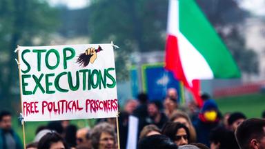 Demonstranten halten ein Schild hoch, auf dem steht stoppt Hinrichtungen, befreit politische Gefangene und tragen eine iranische Flagge.