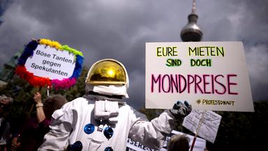 Bei einer Demo hält eine als Astronaut verkleidete Person ein Schild mit der Aufschrift Eure Mieten sind doch Mondpreise.