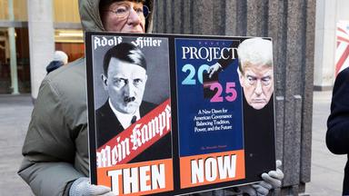 Ein Demonstrant hält ein Plakat, auf dem Hitler und Trump nebeneinander dargestellt sind.